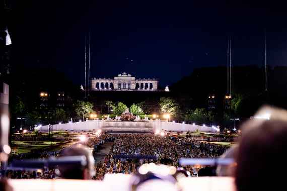 Blick vom Orchester über das Publikum, den Schlosspark und die erleuchtete Gloriette in der Nacht