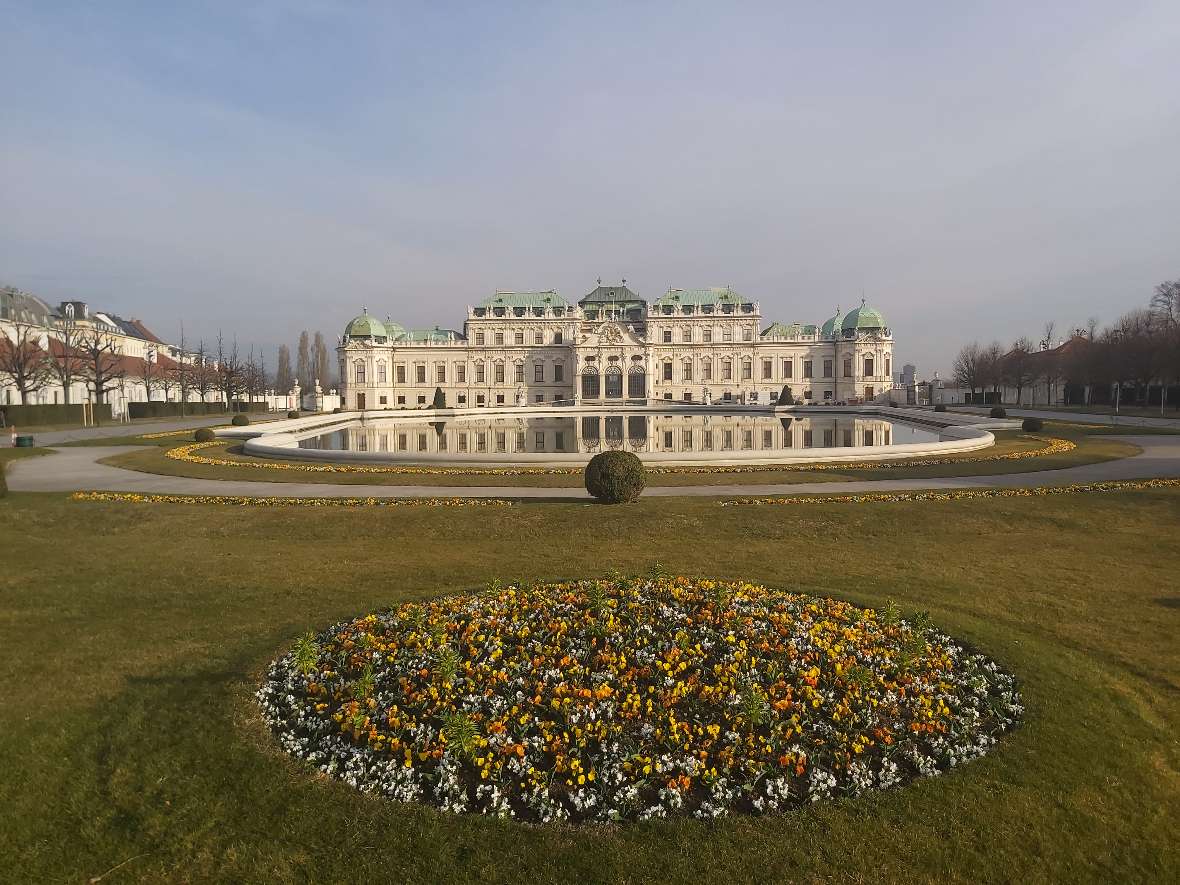 zu sehen sind bunte Blumen in einem Beet, dahinter ein großes helles Gebäude