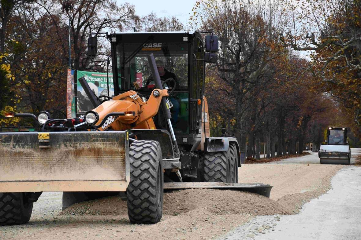 zu sehen ist ein Bagger in dem ein Fahrer sitzt und Kies auf einer Schotterstraße verteilt